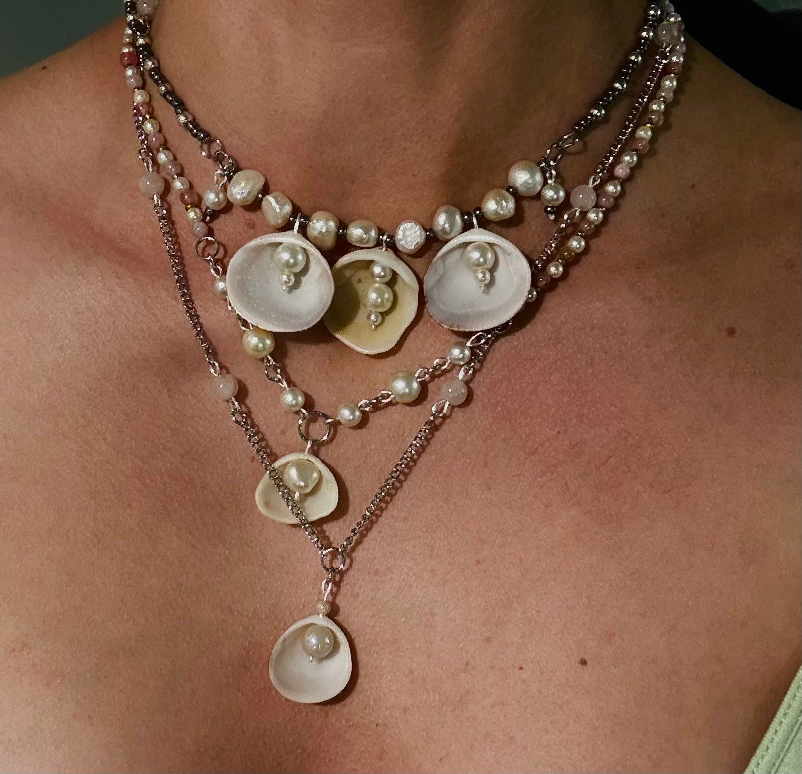 Layered silver chains with pearls and white shell pendants, worn on bare skin.