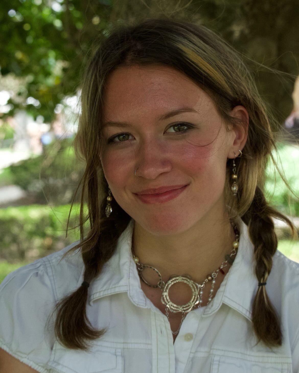 Silver necklace with open circle pendants and pearls, worn with a white collared shirt outdoors.