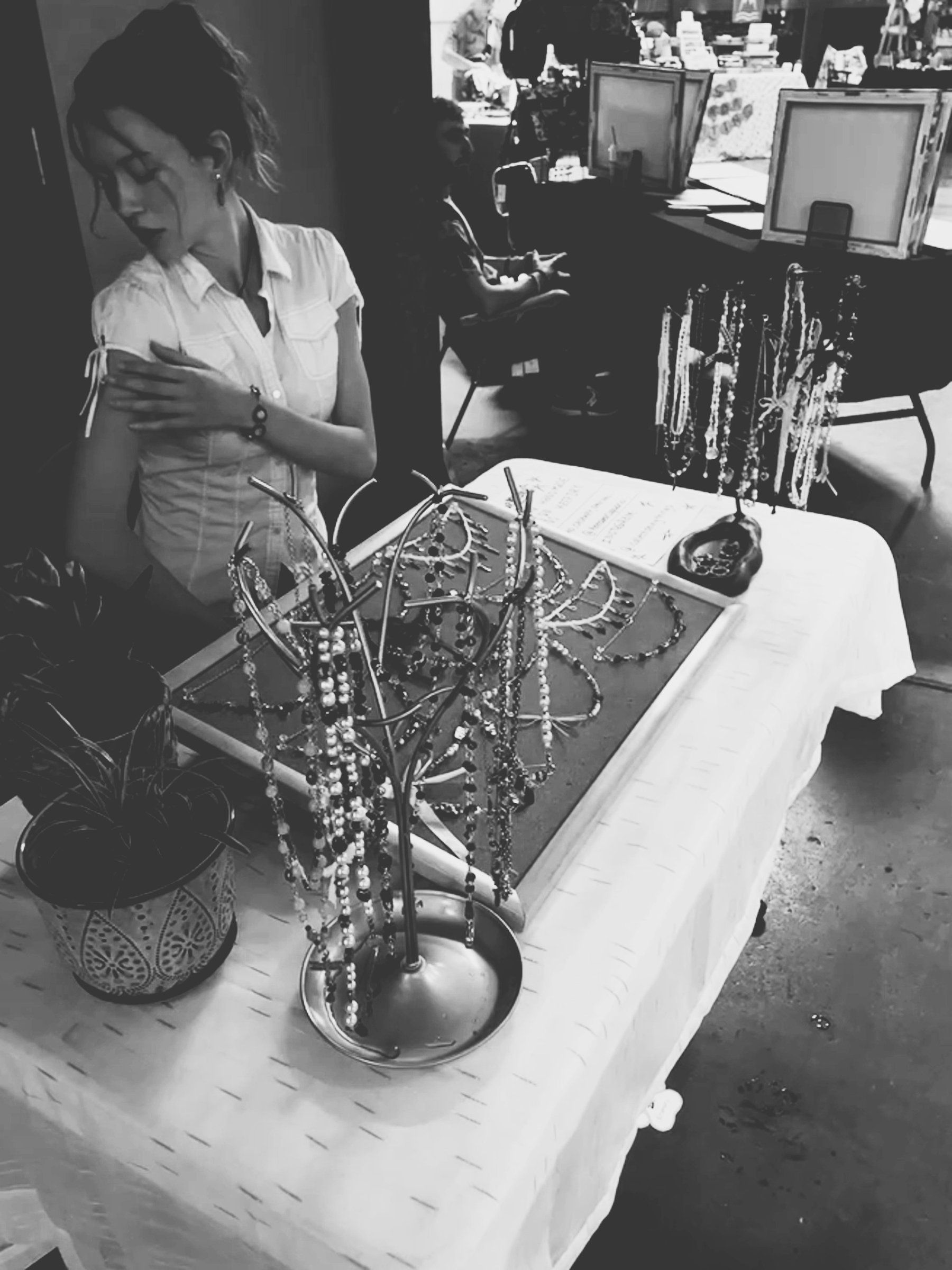 Pop-up shop table with necklaces on a metal jewelry tree and a display board, in black and white.