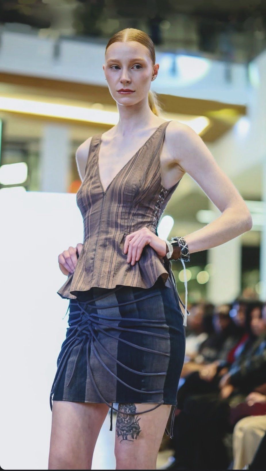 Front view on the runway of the striped brown V-neck peplum top, laced paneled denim skirt, and wrist cuffs.