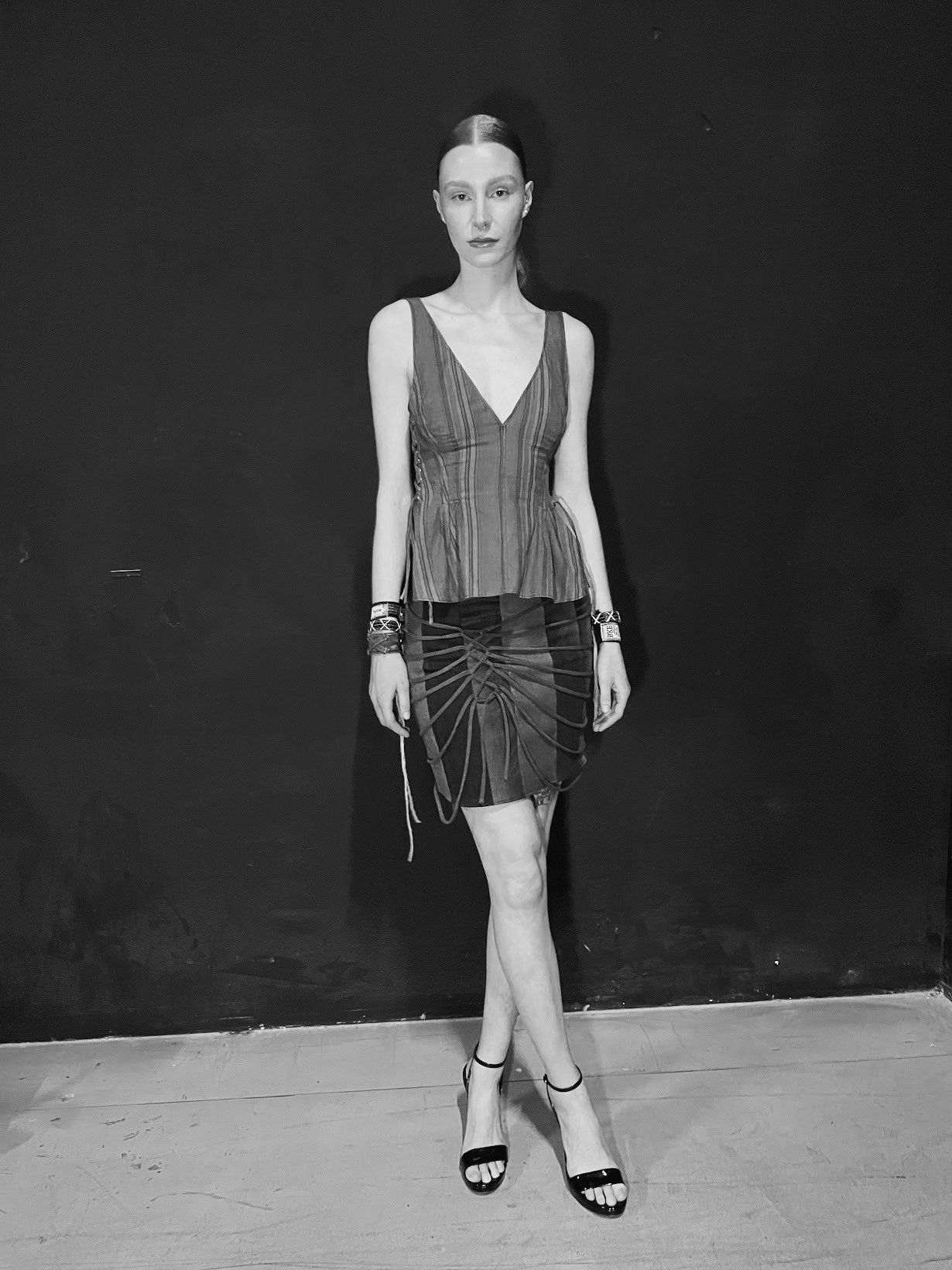 Black-and-white full-length front view of the look against a dark wall, worn with black ankle-strap sandals.