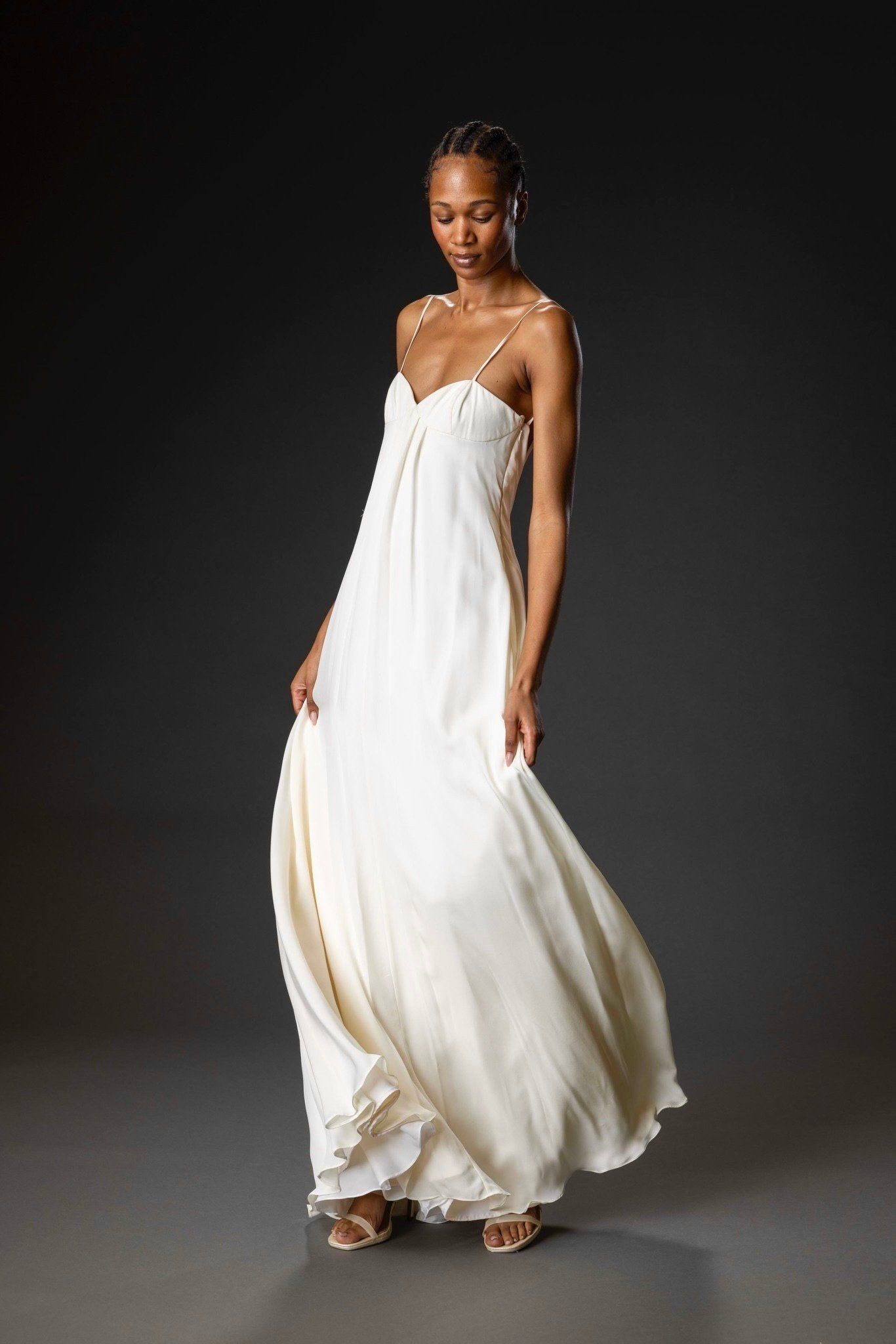 Full-length front view of the ivory silk georgette gown with thin straps and a swirling skirt, on a dark studio backdrop.