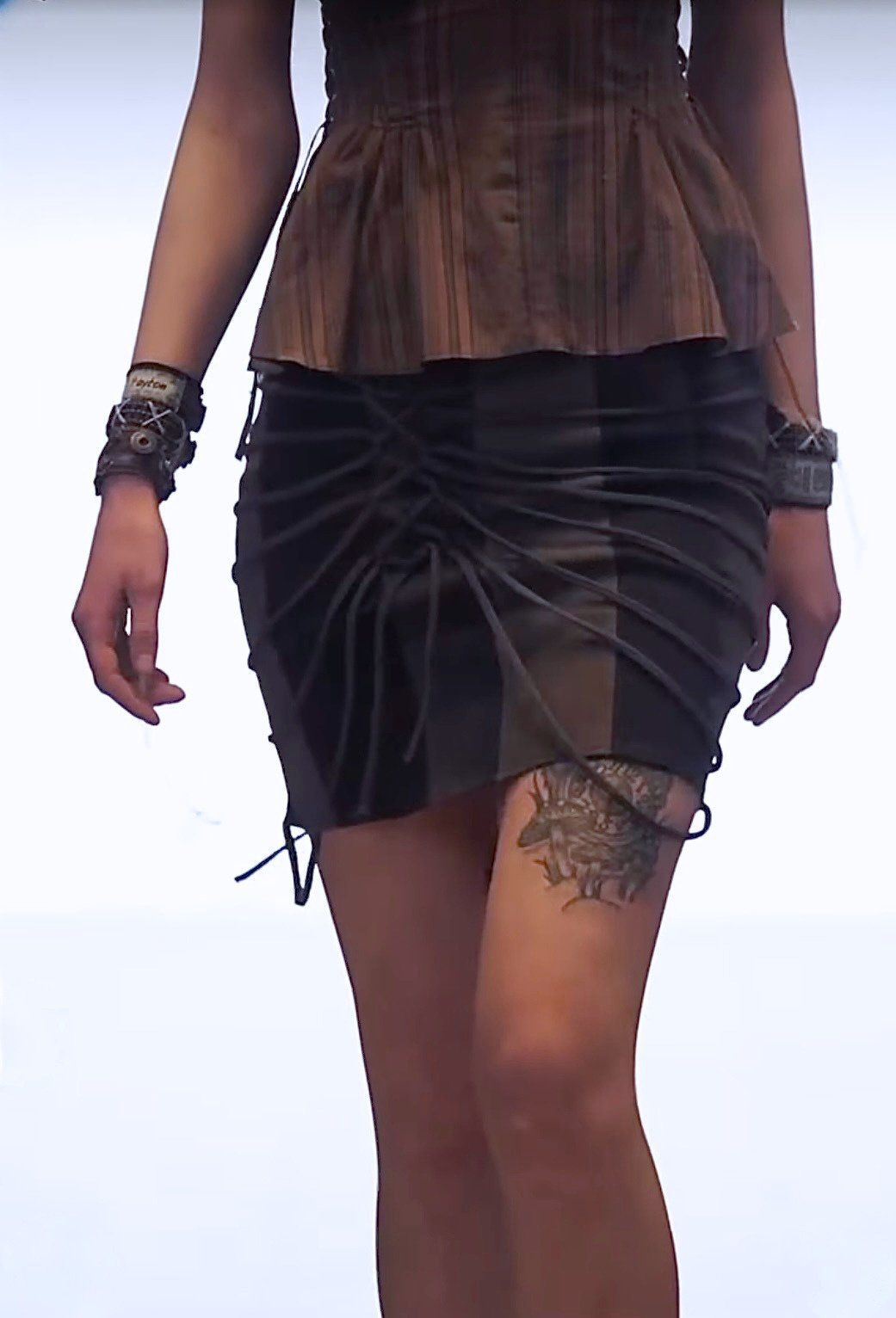 Close-up of the paneled denim skirt with cords wrapped and laced across the front, worn with wrist cuffs.