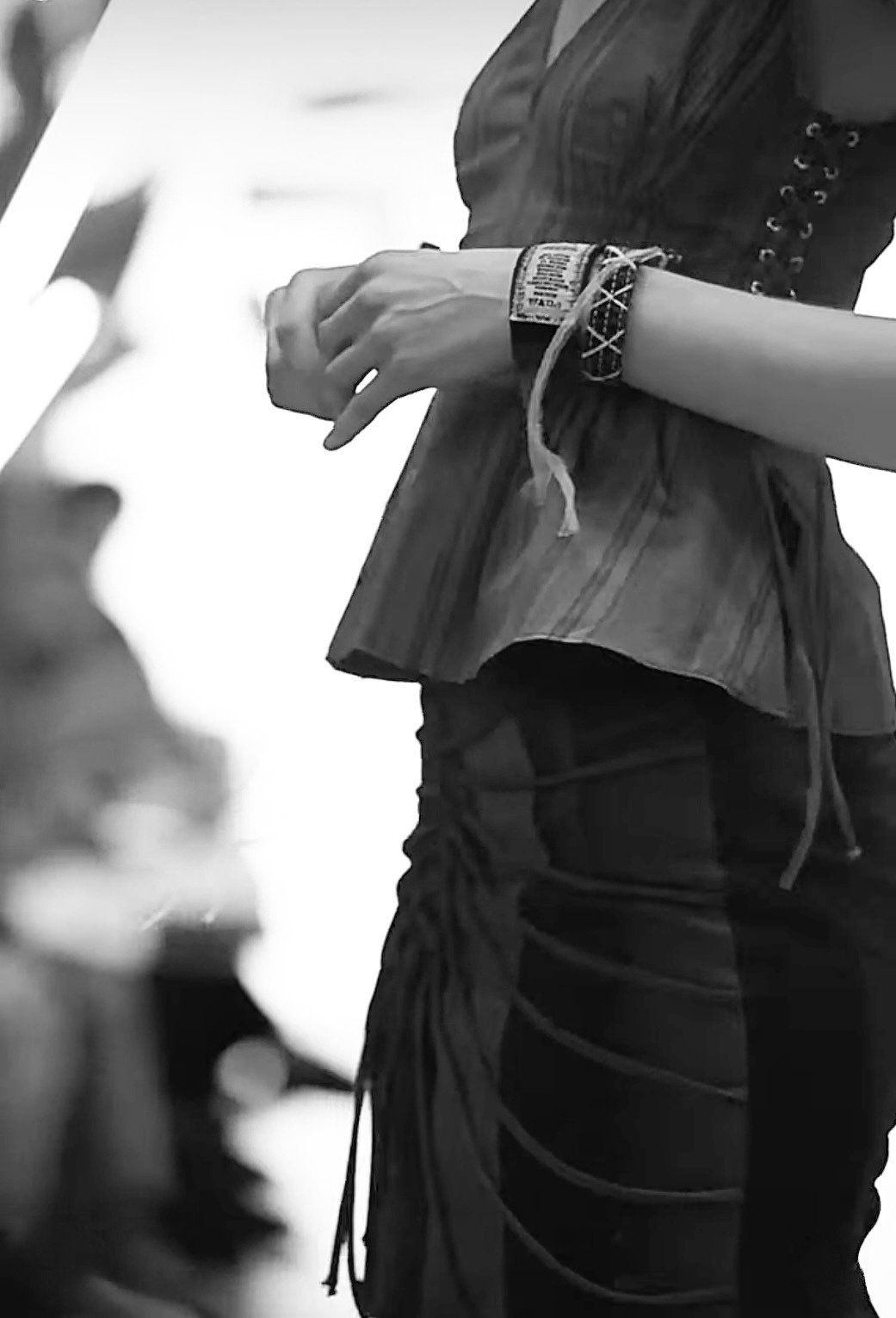 Black-and-white close-up of a laced wrist cuff and the side lacing of the peplum top above the corded skirt.