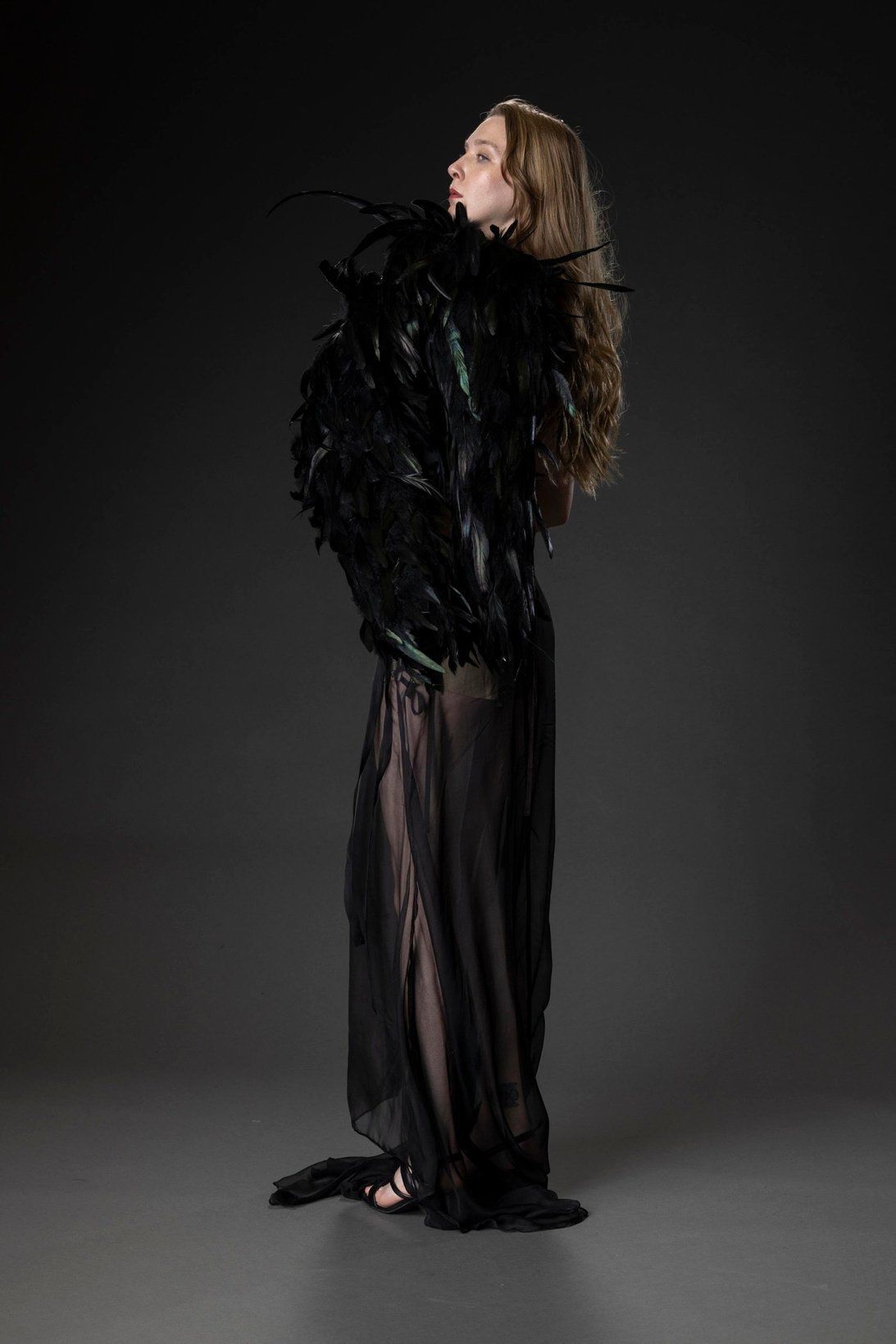 Side profile of the model in Look 2 with the black feather jacket pulled up around her shoulders over the chiffon skirt.