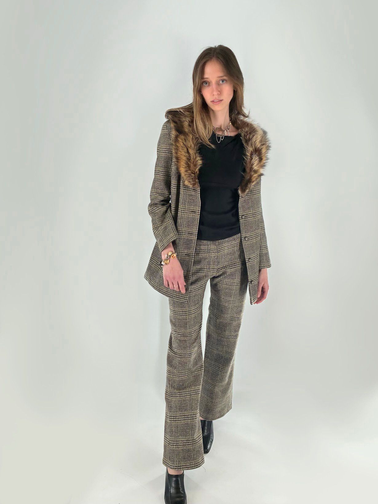 Front view of the brown plaid suit with a fur collar, worn over a black knit top with flared trousers and black ankle boots.