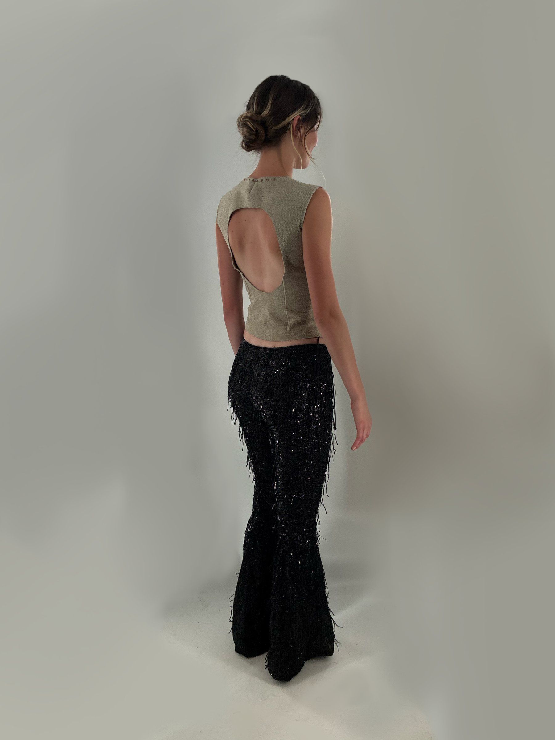 Back view of Look 6: an off-white suede top with a circular back cutout, worn with black sequined fringe flared pants.