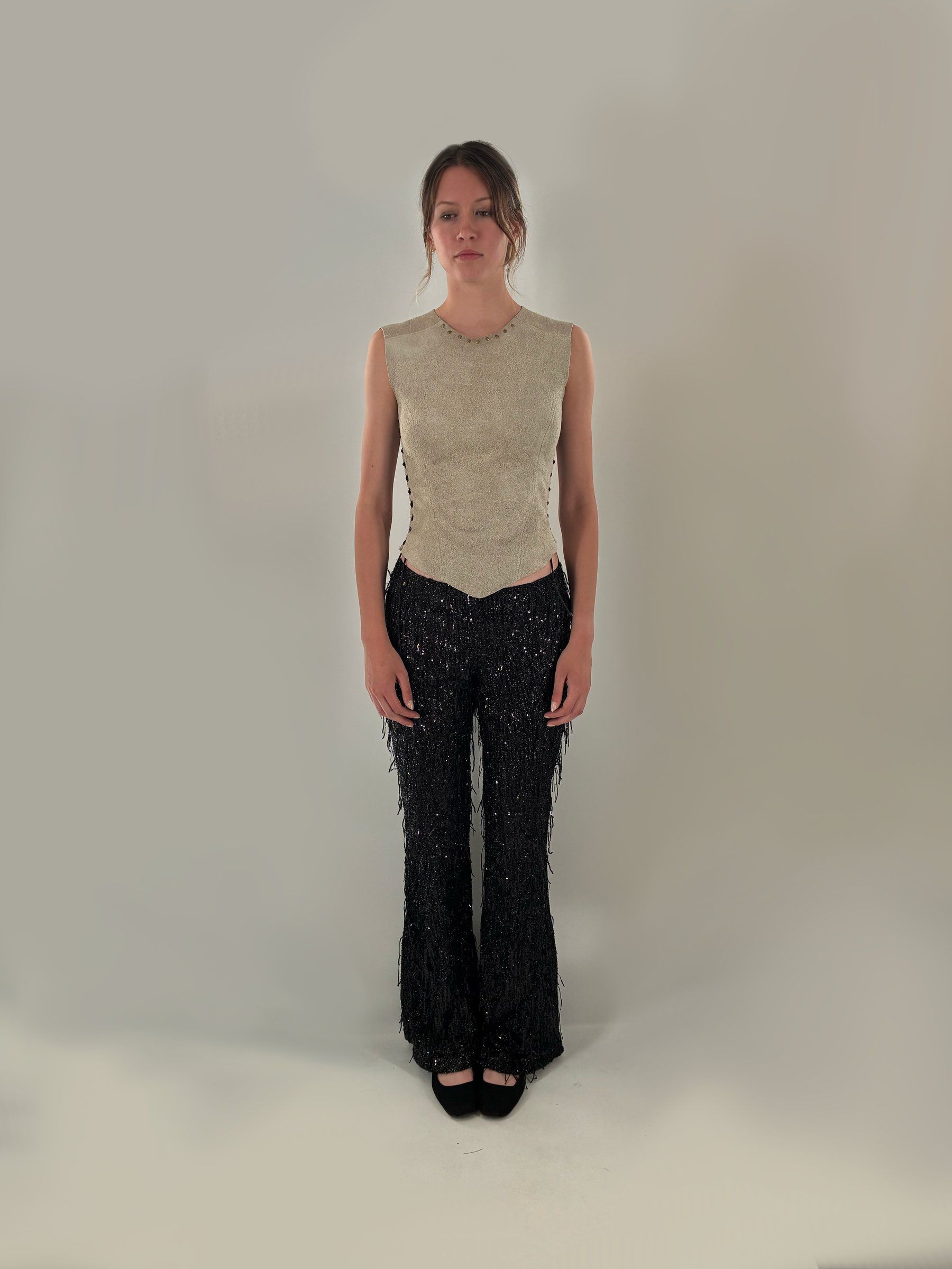 Front view of Look 6: a sleeveless suede top with bronze studs at the neckline and a pointed hem, over black sequined fringe flared pants.