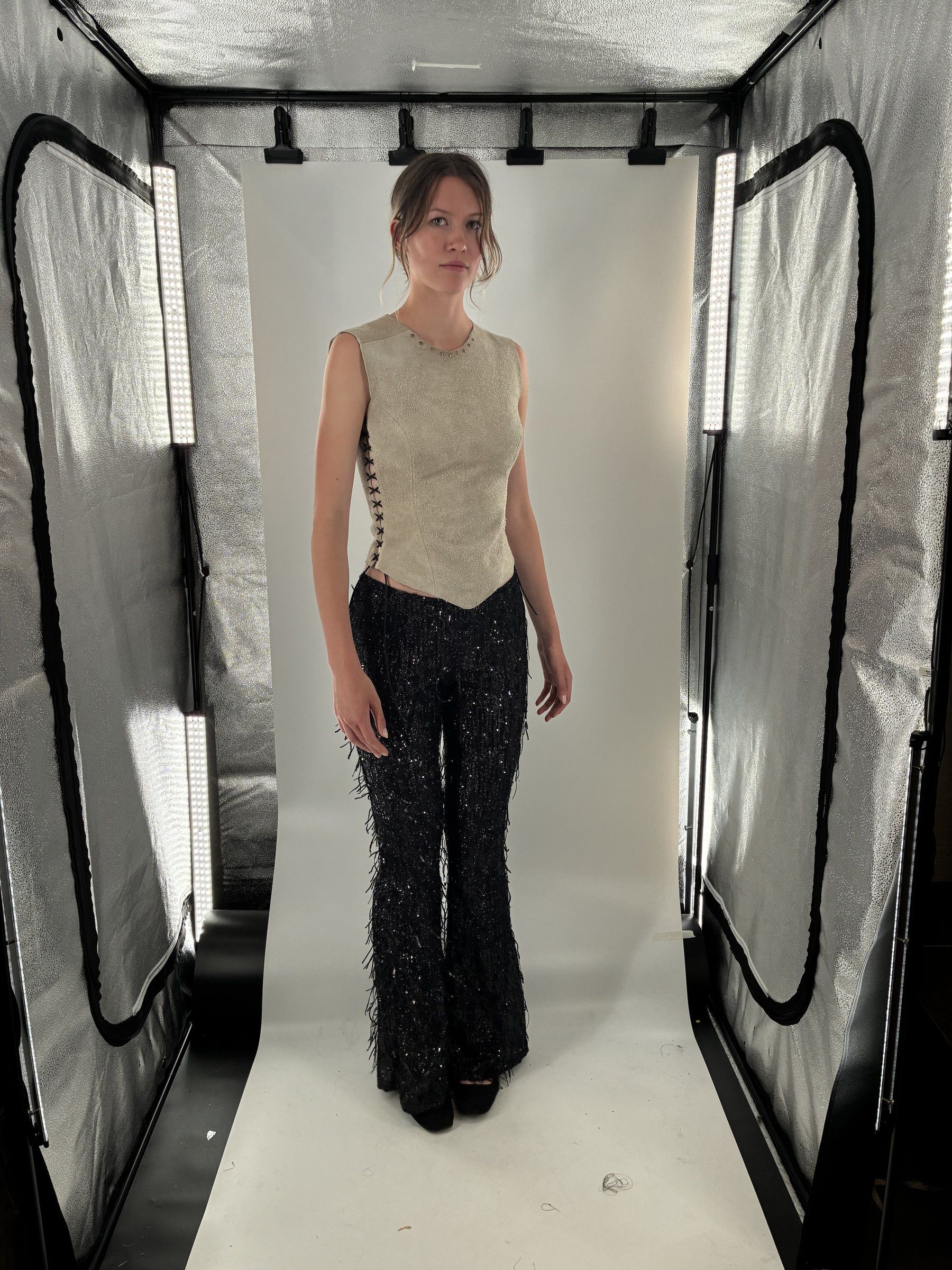 Front three-quarter view of Look 6 in a lit photo tent, showing the suede top's side lace-up and the fringe pants.